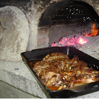 Cabrito assado no forno de lenha em assadeiras de barro preto, com batata assada, arroz de miúdos e grelos salteados.