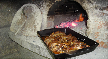 Cabrito assado no forno de lenha em assadeiras de barro preto, com batata assada, arroz de miúdos e grelos salteados.